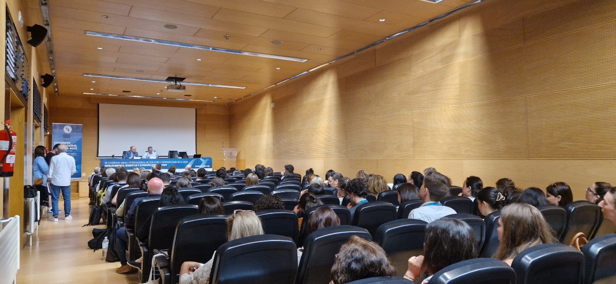 Asistentes en una sala de conferencias durante una ponencia del 35º Congreso de la SGXX, con dos ponentes en mesa al fondo y pantalla de proyección en blanco.