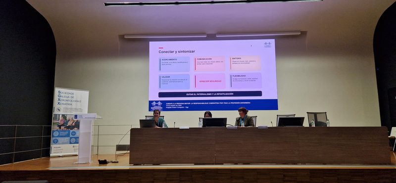 Mesa de ponentes en el salón de actos con la diapositiva «Conectar y sintonizar» proyectada en la pantalla